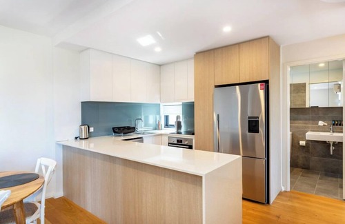 Leederville Apartment | Rooftop Sky Lounge has a daybed, tables and stools, a lounge area with a big screen TV and a grassed