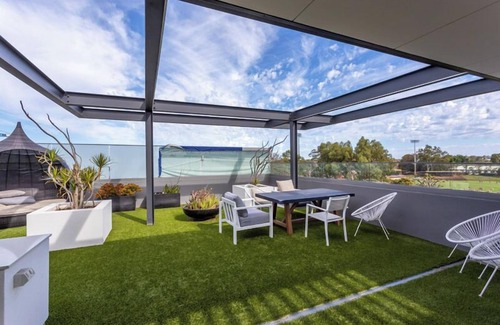 Leederville Apartment | Rooftop Sky Lounge has a daybed, tables and stools, a lounge area with a big screen TV and a grassed